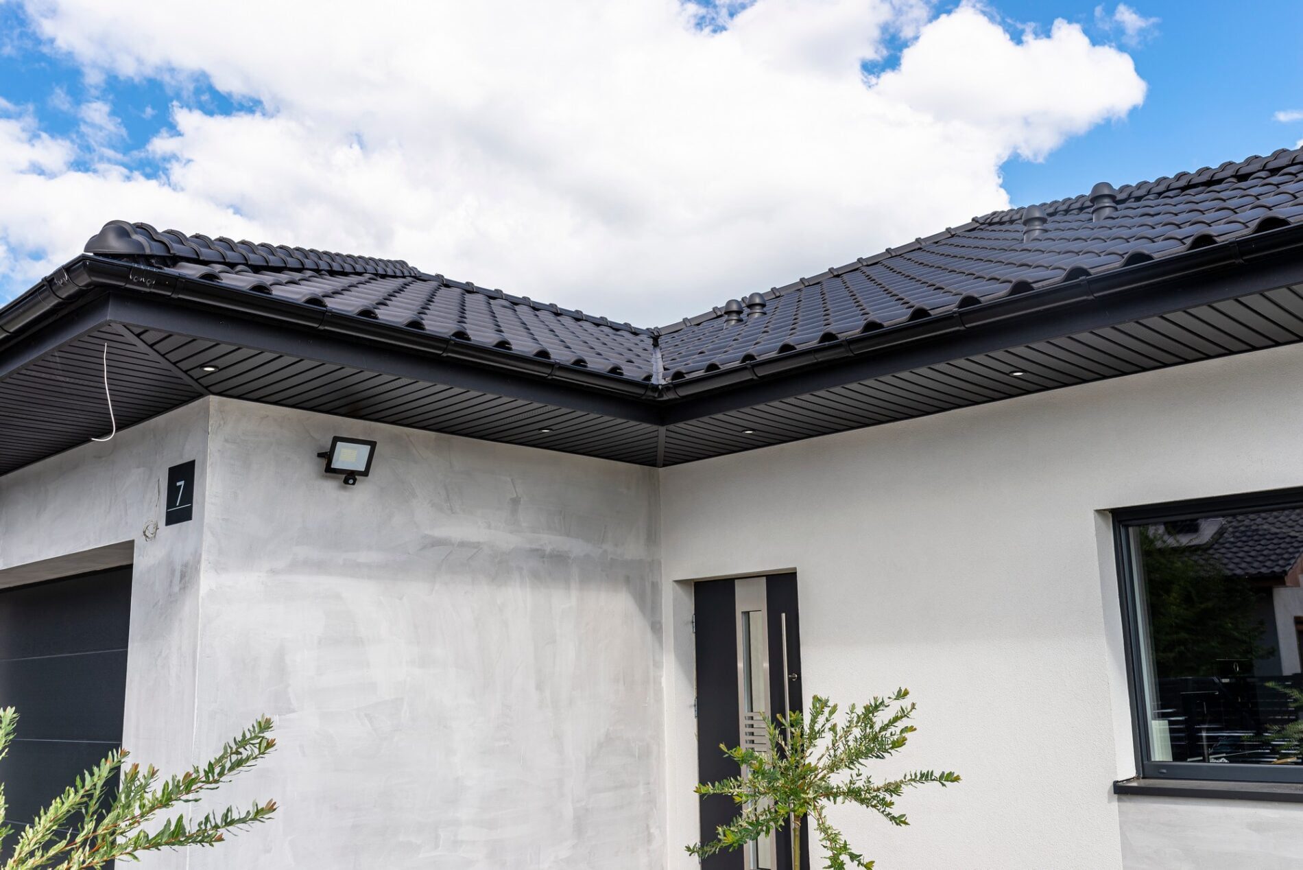 The image showcases a modern roof featuring a sleek, graphite-coloured herringbone pattern. The herringbone design, characterized by its zigzag arrangement, adds an element of intricate detail and contemporary style to the roof. The roofing material appears to be smooth and reflective, creating a clean and uniform appearance. The precise alignment of the pattern underscores high craftsmanship and meticulous installation. Surrounding the roof is a bright, clear sky, which contrasts strikingly with the dark graphite colour, emphasising the modern architectural element and its sharp lines. The overall effect is one of sophistication and modernity, indicative of a well-designed and well-executed roofing project.